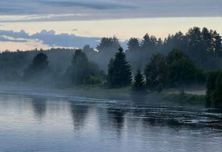 Early morning mist rises over a river by Camping Yttermalungs in Dalarna, Sweden, with pine forest nearby.