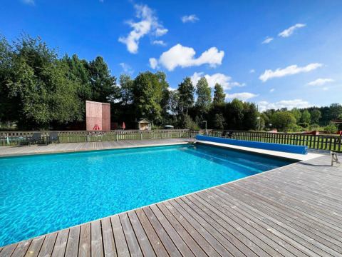 Outdoor swimming pool with wooden deck surrounded by lush greenery at Camping Yttermalungs in Dalarna, Sweden.