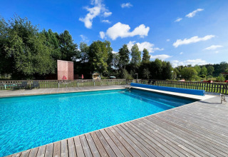 Outdoor swimming pool with wooden deck surrounded by lush greenery at Camping Yttermalungs in Dalarna, Sweden.