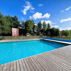 Outdoor swimming pool with wooden deck surrounded by lush greenery at Camping Yttermalungs in Dalarna, Sweden.