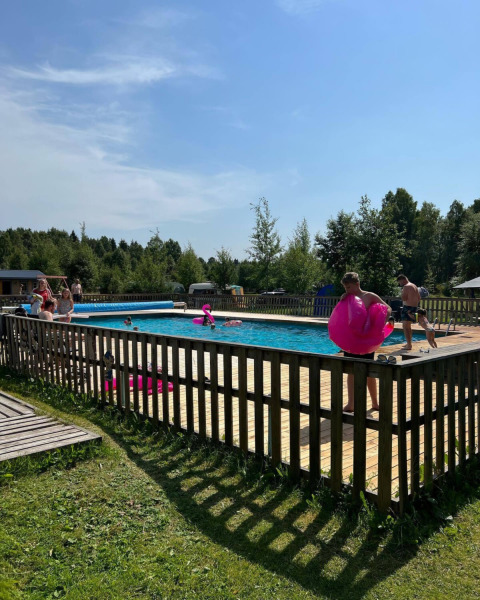 Folk nyder en solrig dag ved en indhegnet swimmingpool på Camping Yttermalungs, Dalarna, Sverige.