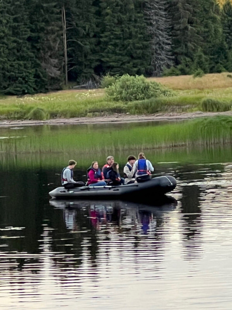 A group of people in a black inflatable boat on a calm lake at Camping Yttermalungs, Dalarna, Sweden.