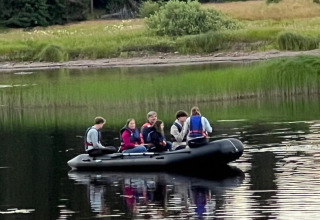 En gruppe mennesker i en sort oppustelig båd på en stille sø ved Camping Yttermalungs, Dalarna, Sverige.