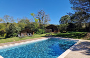 Udendørs swimmingpool foran træhytter og liggestole i det naturskønne Domaine La Sauzette, Occitanie.