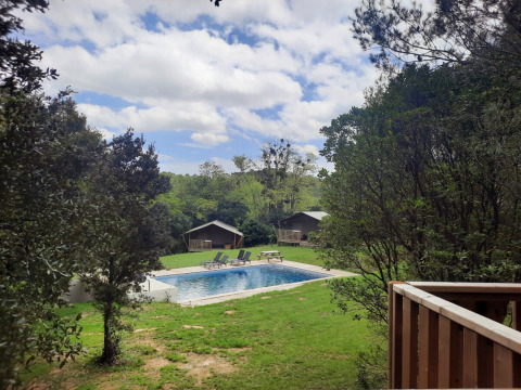 Udsigt over swimmingpool og hytter omgivet af træer på Domaine La Sauzette feriepark i Occitanie, Frankrig.