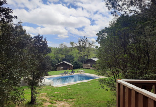 View of pool and cabins surrounded by trees at Domaine La Sauzette holiday park, Occitanie, France.