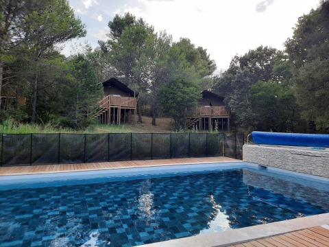 Zwembad met boomhutten op de achtergrond bij Domaine La Sauzette, een vakantiepark in Occitanië, Frankrijk.