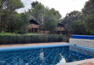 Swimmingpool mit Baumhäusern im Hintergrund im Domaine La Sauzette Ferienpark in Okzitanien, Frankreich.