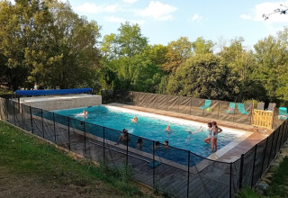 Børn og voksne nyder en svømmetur i poolen omgivet af hegn ved Domaine La Sauzette i Occitanie, Frankrig.