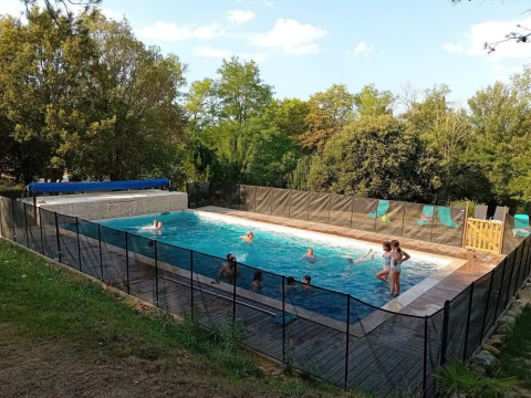 Children and adults enjoy swimming in a fenced pool at Domaine La Sauzette holiday park in Occitanie, France.