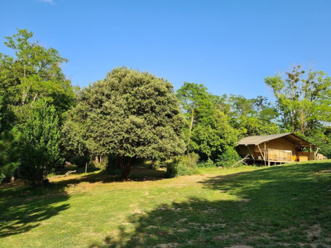 Photo of Domaine La Sauzette holiday park in Occitanie, France, showing a tent and trees under a blue sky.