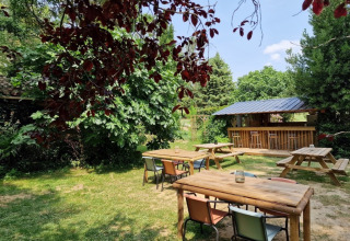 Udendørs siddeområde med træborde, farverige stole og en bar i grønne omgivelser på Domaine La Sauzette.