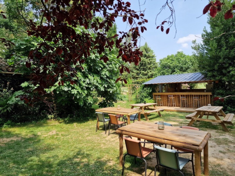 Buitenruimte met houten tafels, kleurrijke stoelen en een bar bij Domaine La Sauzette in Occitanië.