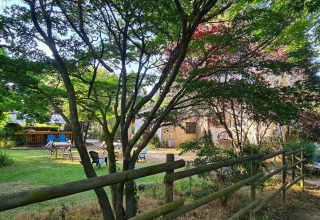 Grüner Garten mit Bäumen, Holzzaun und Gartenmöbeln im Domaine La Sauzette, Occitanie, Frankreich.