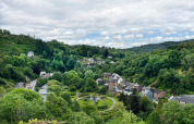 Panoramic view of green hills, river, trees, and houses at Camping la Roche holiday park in Limburg, Belgium.
