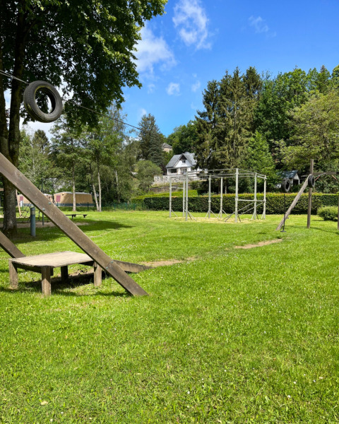 Legeplads med gynger og grønne træer på Camping la Roche, feriested i Limburg, Belgien, på en solrig dag.