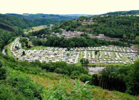 View of Camping la Roche holiday park in Belgian Limburg with caravans, town, river, and forested hills.