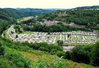 Vista sul Camping la Roche a Limburg, Belgio, con roulotte, piccolo paese e colline verdi e boscose.