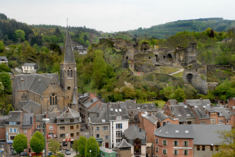 View of a Belgian town with a church, castle ruins, and surrounding green hills and trees in spring.