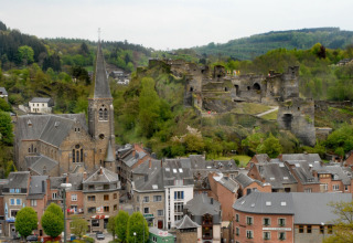 View of a Belgian town with a church, castle ruins, and surrounding green hills and trees in spring.