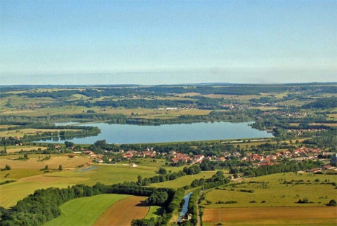 Aerial view of Camping du Lac in Grand Est, France, showing a lake, fields, and nearby villages.