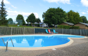 Udendørs swimmingpool med liggestole og hegn, omgivet af træer, campingvogne og hytter på Camping du Lac.