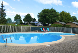 Round swimming pool with lounging chairs at Camping du Lac holiday park, Grand Est, France, on sunny day.