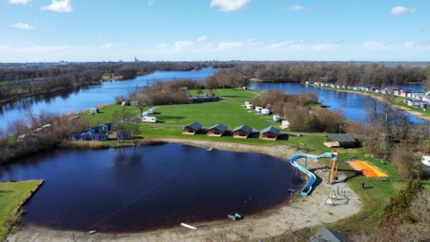 Aerial view of Camping de Kleine Wielen in Friesland, Netherlands, featuring a lake and playground slide.