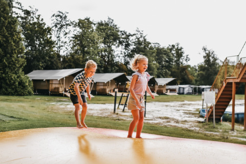 Dos niños juegan en una gran colchoneta inflable en Camping de Kleine Wielen, parque de vacaciones en Friesland.