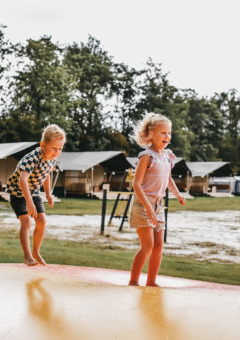 Dos niños juegan en una gran colchoneta inflable en Camping de Kleine Wielen, parque de vacaciones en Friesland.