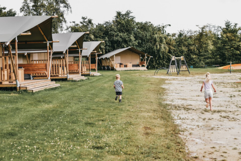 Des enfants jouent dehors près de tentes safari et d’une aire de jeux à Camping de Kleine Wielen, Friesland.