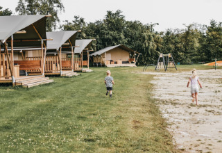 Des enfants jouent dehors près de tentes safari et d’une aire de jeux à Camping de Kleine Wielen, Friesland.