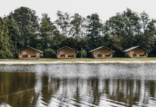 Quattro tende glamping al Camping de Kleine Wielen in Frisia, Paesi Bassi, riflesse su un lago calmo.