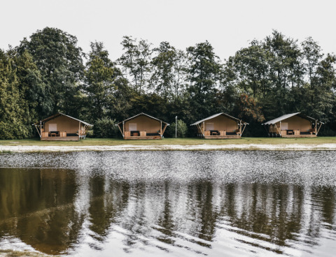 Vier Glamping-Zelte am Camping de Kleine Wielen in Friesland, Niederlande, spiegeln sich im Wasser.
