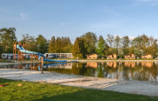 Panorama sul lago con scivolo d’acqua e bungalow a Camping de Kleine Wielen, Friesland, Paesi Bassi.