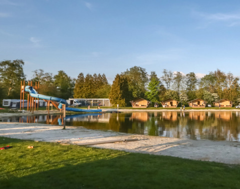 Blick auf einen See mit Rutsche und Ferienhütten im Camping de Kleine Wielen, Friesland, Niederlande.