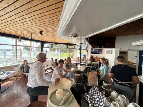 Clients discutent dans un café lumineux avec vue sur le port à Minicamping Marina Warns, aux Pays-Bas.