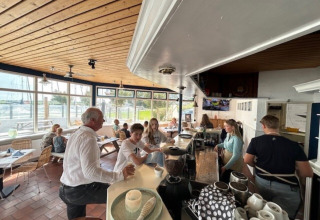 Guests socializing at a cozy café with harbor view inside Minicamping Marina Warns, Friesland, Netherlands.