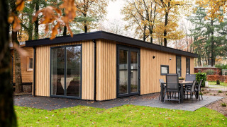 Moderne lodge genaamd Module Wood met houten gevelbekleding, grote ramen en buitenterras in het groen.