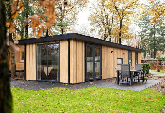 Moderne lodge Module Wood met houten bekleding, grote ramen en buitenterras midden in het groen.