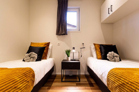 Modernes Zimmer mit zwei Einzelbetten, goldenen Kissen und Fenster in der Module Wood Lodge, Niederlande.
