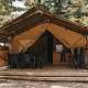 Tente safari avec sanitaires, terrasse en bois, table à manger et chaises dans un cadre boisé.