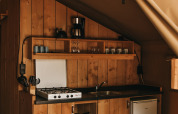 Cuisine sous tente safari avec panneaux bois, gazinière, évier, cafetière et mini-frigo à Camping Lucherino.