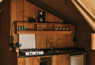 Cuisine sous tente safari avec panneaux bois, gazinière, évier, cafetière et mini-frigo à Camping Lucherino.
