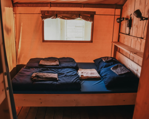 Innenaufnahme eines Safari-Zeltes mit Doppelbett, dunkler Bettwäsche und Fenster auf Camping Lucherino in Italien.