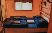Binnenkant van een safaritent met een tweepersoonsbed, donker dekbed en raam op Camping Lucherino in Italië.