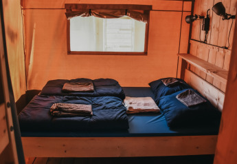 Interno di una tenda safari con letto matrimoniale, biancheria scura e finestra al Camping Lucherino in Italia.