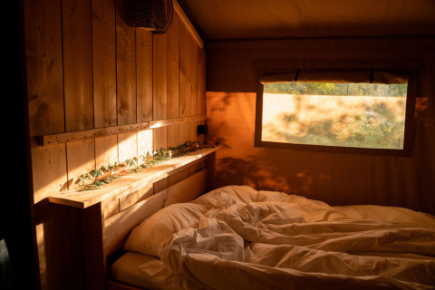 Sonnenlicht fällt in ein gemütliches Schlafzimmer mit Holzwänden in einem Safarizelt bei Jocomo Parc, Belgien.