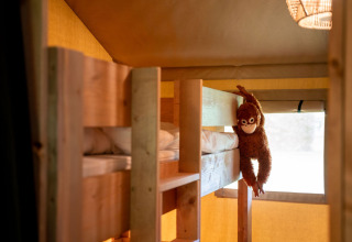 Interior de tienda safari en Jocomo Parc, Bélgica, con literas de madera y un mono de peluche colgando.