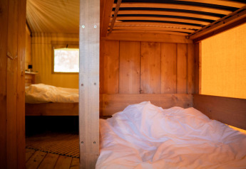 Vista interior de la tienda Safari con sanitarios en Jocomo Parc, Bélgica, mostrando literas de madera.